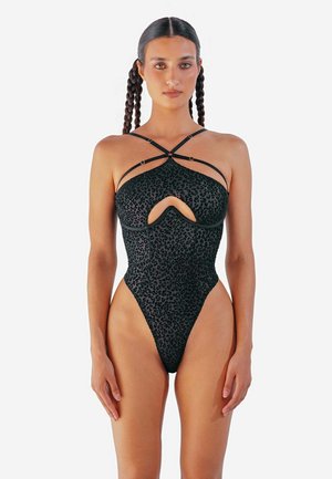 Costume da bagno con stampa di leopardo nera, caratterizzato da gambe alte e spalline incrociate. La parte superiore presenta un taglio anteriore e un tessuto testurizzato.