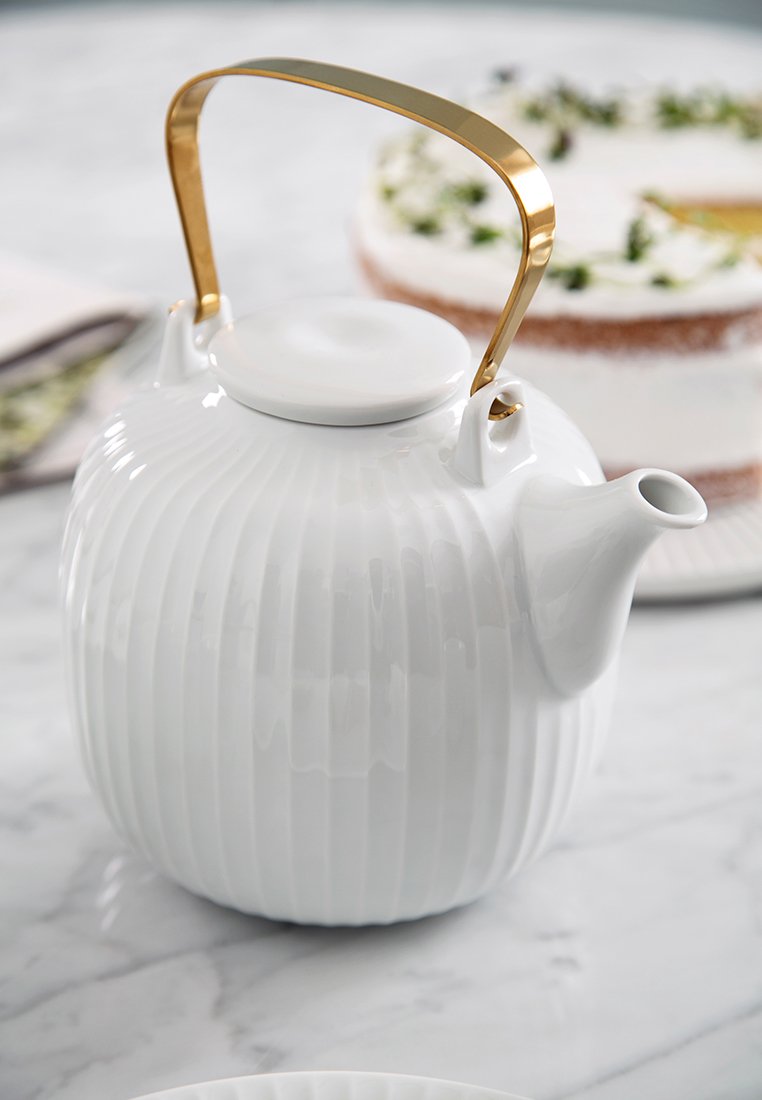 Biała porcelanowa czajnik z pionowym prążkowaniem, zaokrąglonym kształtem i złotym metalowym uchwytem. Posiada dzióbek i dopasowaną pokrywkę.