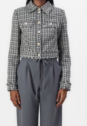 Schwarz-weißes Tweed-Cropped-Jäckchen mit Perlenknöpfen, kombiniert mit hoch taillierter grauer Hose, die in der Taille gebunden ist.