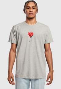 Grå bomuld t-shirt med korte ærmer, der har et grafisk motiv af en rød hjerteformet ballon med gule stjerner og en sort snor detalje.