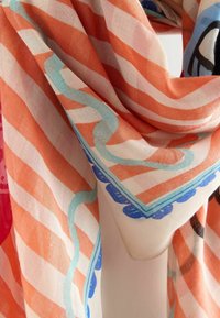 Viegls šalle ar oranžām un baltām slīpajām svītrām, gaisīgi ziliem un ziliem dekoratīviem malām, pārkārta un plūstoša.