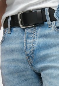 Φωτεινό μπλε τζιν με ξεθωριασμένο φινίρισμα, φορεμένο με μαύρη δερμάτινη ζώνη που διαθέτει ασημένια αγκράφα και υφή σχεδίου.