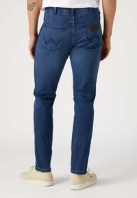 Jeans de mezclilla azul oscuro con un corte ajustado, que cuentan con dos bolsillos traseros con costuras decorativas y una etiqueta negra encima del bolsillo derecho.