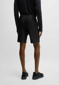 Shorts de sport noirs avec une texture lisse, de longueur standard et une taille élastique. Portés avec des chaussures de sport noires. Design minimaliste.