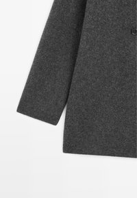 Cappotto di lana grigia con una texture morbida, dotato di un ampio colletto e un unico bottone nero, taglio dritto con manica lunga.