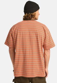 Stripet t-shirt med vandrette mønstre i orange, hvid og grøn. Korte ærmer, afslappet pasform, lavet af blødt bomuldsstof.