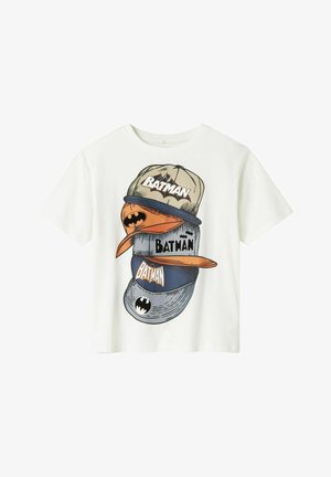 Biała koszulka z grafiką przedstawiającą ułożone na sobie czapki bejsbolowe w kolorach beżowym, pomarańczowym i niebieskim, z napisem "BATMAN" i symbolami nietoperza.