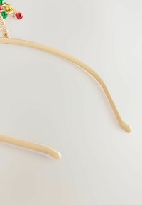 Beige Brillenfassungen mit einer kleinen dekorativen goldenen Feder und grünen, roten und goldenen Glocken, die auf einer Seite befestigt sind.