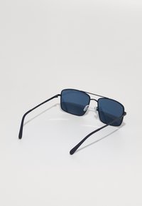 Ochelari de soare pătrați cu lentile de un albastru închis, ramă subțire din metal negru și pernuțe nazale ajustabile, având un design elegant și minimalist.