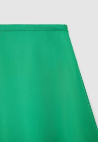 Grüner Stoff mit glatter Textur, der oben mit einem Reißverschluss versehen ist. Das Design hat eine dreieckige Form, die Einfachheit und Farbe betont.