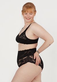 Zwart kanten bh met zachte cups en dunne bandjes, gecombineerd met hoog-waist kanten slipjes met bloempatronen en gegolfde randjes.