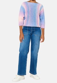 Pletený, vícebarevný svetr v pastelových odstínech růžové a modré, doplněný širokými modrými džíny a bílými teniskami.