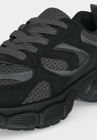 Basket de sport noire et grise avec des panneaux en mesh, une semelle épaisse texturée et des lacets gris, vue rapprochée de face et de côté.