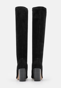 Botas negras hasta la rodilla hechas de suave ante, con una textura lisa, un tacón robusto y detalles de costura mínimos.