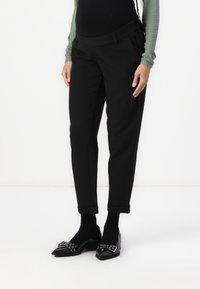 Pantalons fuselés noirs avec une texture lisse, dotés d'une taille et de revers roulés. Associés à des ballerines noires brillantes et des chaussettes noires.
