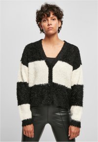 Svart och vit randig fluffig cardigan med djup V-ringning, långa ärmar och framknappar, ihop med svarta åtsittande byxor.