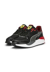 Zapatillas deportivas negras con una combinación de cuero y malla, con acentos rojos, una franja gris y un logo amarillo de Ferrari en la lengüeta.