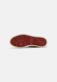 Sneaker-Sohle aus Gummi mit einer strukturierten roten Oberfläche, kreisförmigen und linearen Mustern sowie einem beigen Rand.
