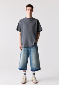 Szürke, oversized póló, laza kék farmer culotte nadrág szaggatott széllel, fehér és krém színű sportcipők, csíkos zoknik, többrétegű fém láncok.