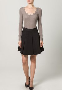 Sivi pleteni bodi s valovitim izrezom, uparen s crnom nabrano nabrano suknjom s naborima. Oba odjevna predmeta imaju duge rukave.