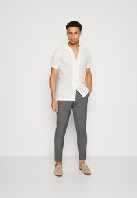White short-sleeve shirt with eyelet pattern, paired with slim-fit gray pants and light beige loafers. Smooth texture, casual design.
