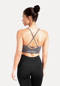 Grijze sportbeha met gekruiste bandjes, voorzien van een logo bij de zoom, gecombineerd met zwarte leggings met hoge taille. Soepele textuur, nauwsluitend ontwerp.