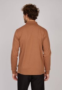 Polo-shirt marron à manches longues avec col et ourlet droit. Texture lisse avec une étiquette sur le côté gauche. Design simple. Sans motifs.