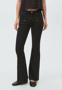 Los jeans negros acampanados presentan detalles metálicos, un diseño de costura curvada, dos bolsillos frontales y un dobladillo ligeramente deshilachado para dar textura.