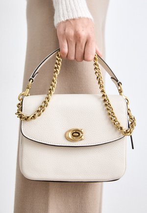 Bílá kožená kabelka se zlatým řetízkem, s kulatým klopou a zlatým uzávěrem. Hladký povrch s černými okraji.