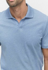 Ljusblå polo skjorta med texturerad vikt, korta ärmar och en klassisk spetsig krage. Har en treknapps öppning och en subtil lyster.