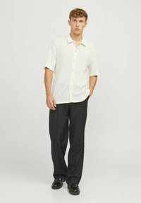 Korte mouwen, lichtgekleurde shirt met verticale ribbeling en knopen, gecombineerd met zwarte broek en glanzende zwarte schoenen.
