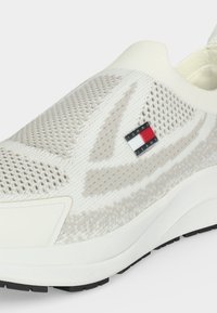 Baskets blanches en maille à enfiler avec empeigne texturée, semelle blanche épaisse, semelle extérieure noire et petit logo Tommy Jeans sur le côté.