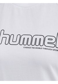 Hvid T-shirt med et iøjnefaldende sort logo "hummel" og sloganet "FORANDR VERDEN GENNEM SPORT." Blødt bomuldsstof, rund halsudskæring, minimalistisk design.