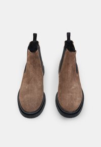 Rudi suediniai Chelsea batai su juodais elastingais įdėklais ir tempimo kilpomis, su struktūrizuotu juodu guminiu padu. Viršuje matomas dizaino detalės.