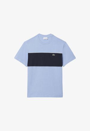 Camiseta azul claro de manga corta con una amplia franja negra horizontal en el pecho y un pequeño logotipo de cocodrilo verde en el lado izquierdo.