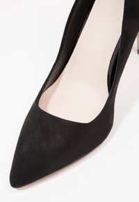 Chaussure noire en suède à talon haut avec un bout pointu et un décolleté bas, dotée d'une doublure intérieure couleur naturelle et d'un talon aiguille.