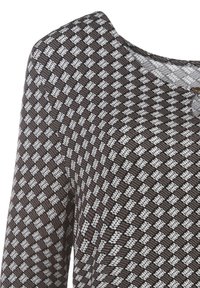 Braun- und weiß gemusterte Bluse mit rundem Ausschnitt, die ein geometrisches Diamantdesign und einen kleinen Knopfakzent aufweist. Weicher Stoff.