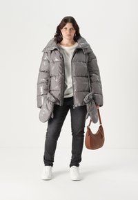Sivi puffer jakna sa sjajnim završetkom, podstavljenim dijelovima, pripadajućim rukavicama i velikim kapuljačom. Uparena s tamnim trapericama i smeškim torbicom.