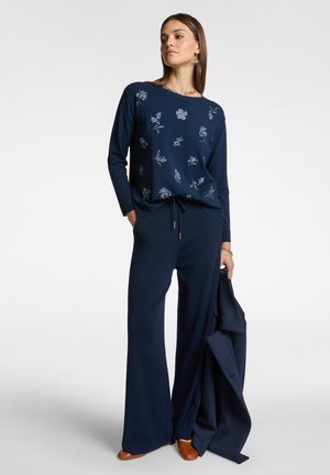 Maglione navy con ricami floreali in tonalità più chiare, abbinato a pantaloni navy a gamba larga. Tessuto liscio con coulisse e dettagli hardware minimi.
