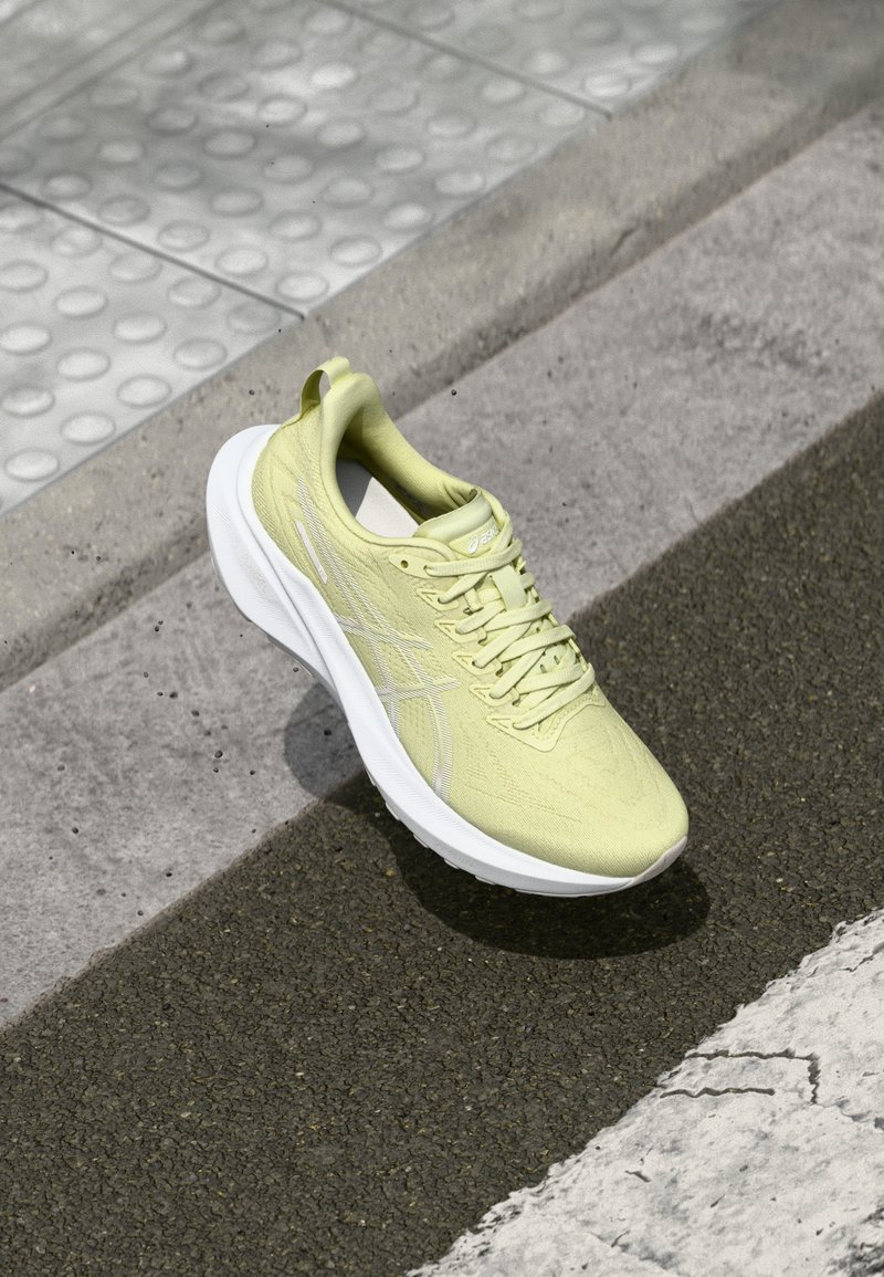 Chaussure de sport jaune clair avec une tige texturée, semelle blanche et lacets. Bout arrondi et languette au talon ; détail de marque minimal.