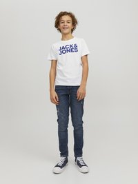 Camiseta blanca de manga corta con el texto azul "JACK & JONES", combinada con jeans de mezclilla azul oscuro y zapatillas marinas con suelas blancas.