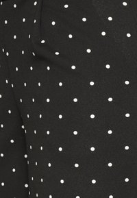 Czarna tkanina z równomiernie rozmieszczonymi małymi białymi kropkami, ukazująca fakturę i drobne zmarszczki.