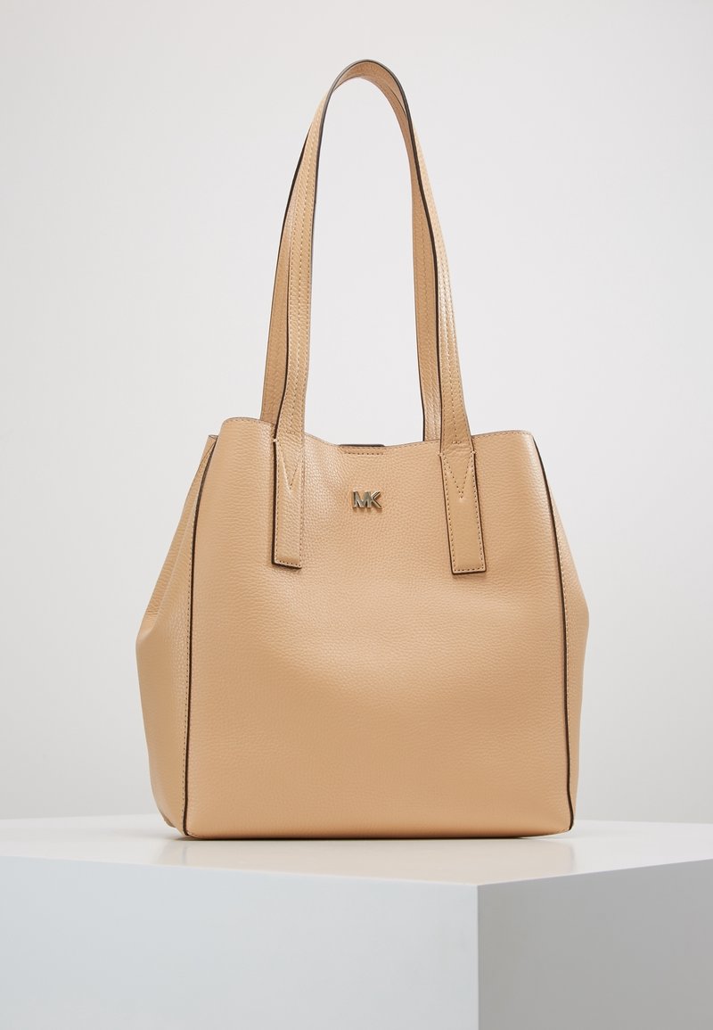 Sac cabas en cuir beige Michael Kors avec deux bretelles d'épaule et petit logo doré « MK » sur le devant, présenté sur une surface blanche.