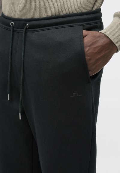 Μαύρο παντελόνι φόρμας κατασκευασμένο από απαλό υλικό, με πλαϊνές τσέπες, κορδόνι στο κλείσιμο και μίνιμαλ λογότυπο στο μηρό.