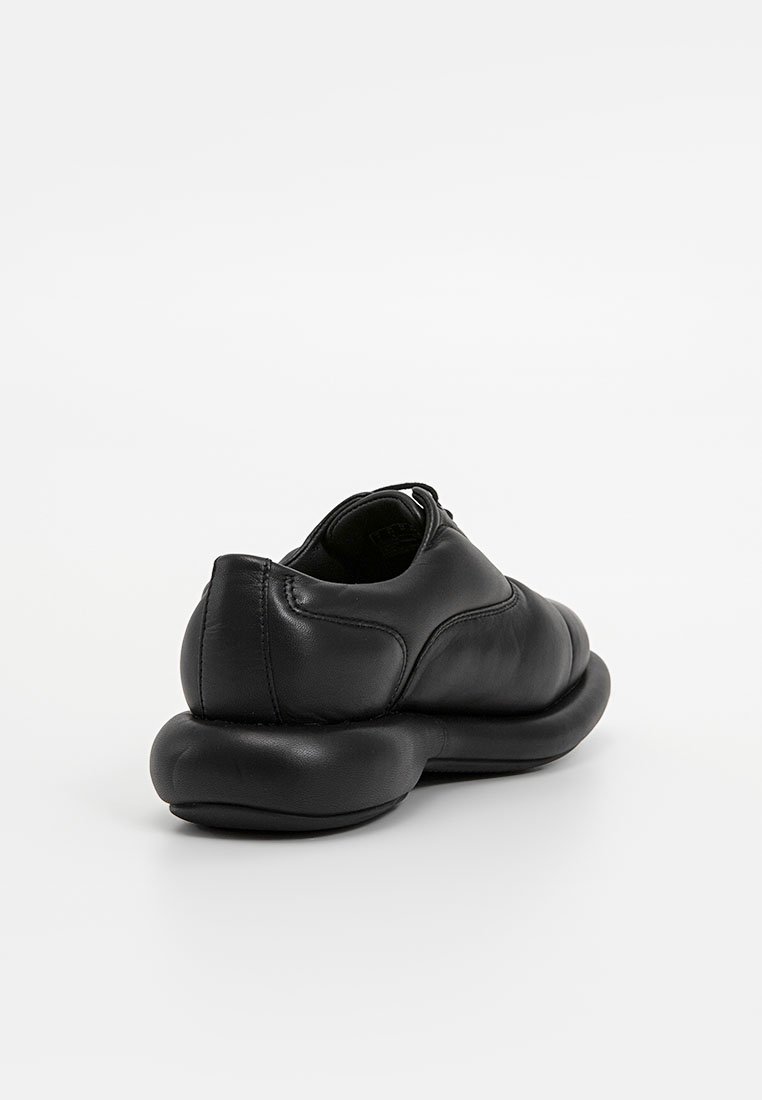 Chaussure noire en cuir au design arrondi, texture lisse et semelle rembourrée. Présente un petit talon et des détails de couture minimalistes.