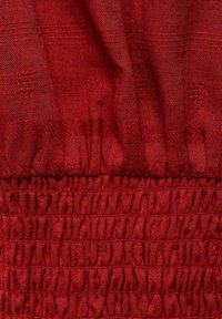 Röd tyg med en texturerad yta och ett samlat elastiskt midjeband. Materialet är lättviktigt och har en subtil lyster.