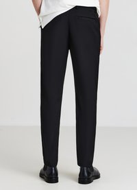 Pantaloni neri con vestibilità slim, texture liscia e una tasca posteriore singola. Abbinati a una camicia e scarpe nere, mostrati da dietro.