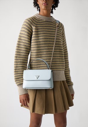 Borsa in pelle azzurro chiaro con manico superiore e tracolla a catena. Presenta una chiusura a pattina e un logo triangolare. Indossata con un maglione a righe e una gonna.