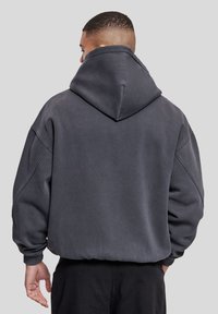 Sweat à capuche surdimensionné gris foncé en tissu doux, doté d'une grande capuche, d'épaules tombantes et de poignets côtelés, avec une texture lisse.