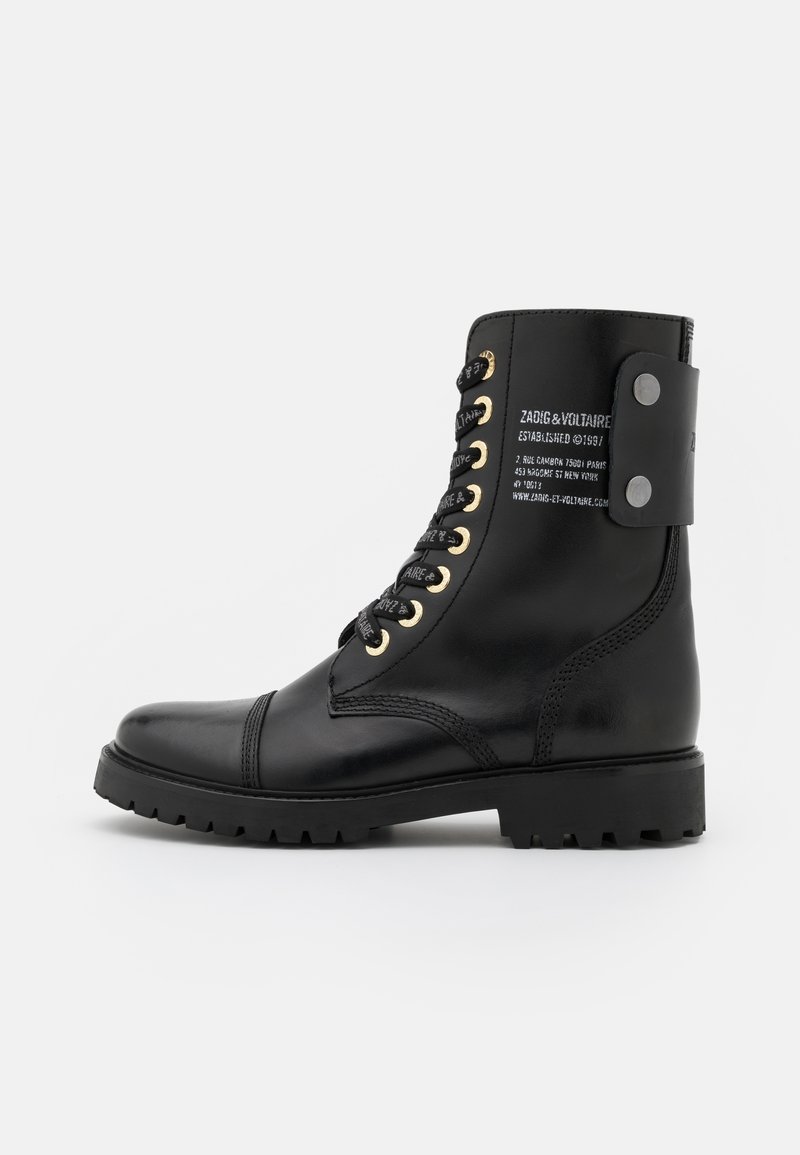 Black leather combat boot with gold eyelets, black laces, and a back strap detail featuring printed text. Thick, textured rubber sole.